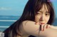 A woman with long brown hair sitting on a bench by the ocean.