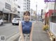 A woman in a blue top and plaid skirt standing on a street.